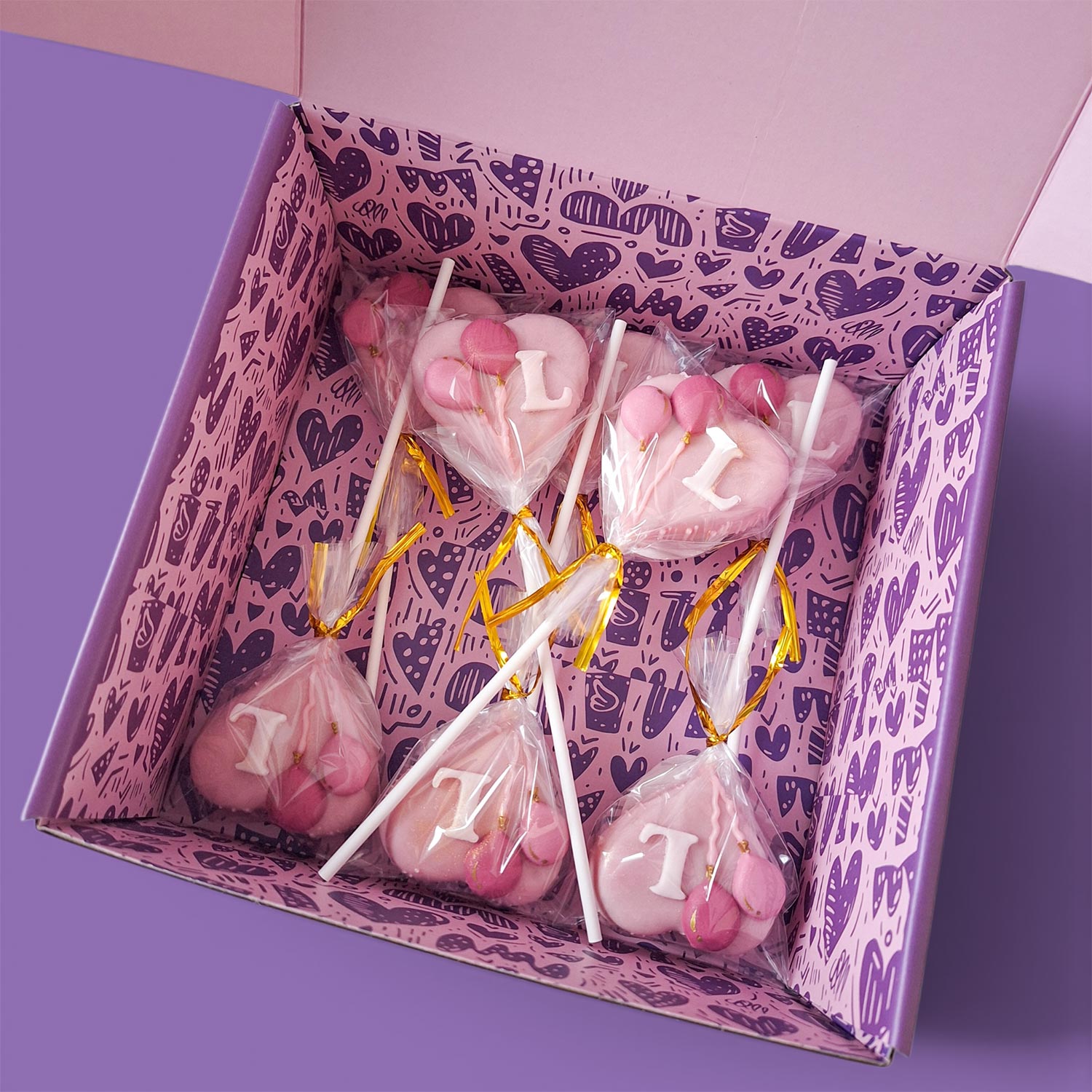 Box of Pink Cake Pops with letters and balloons.