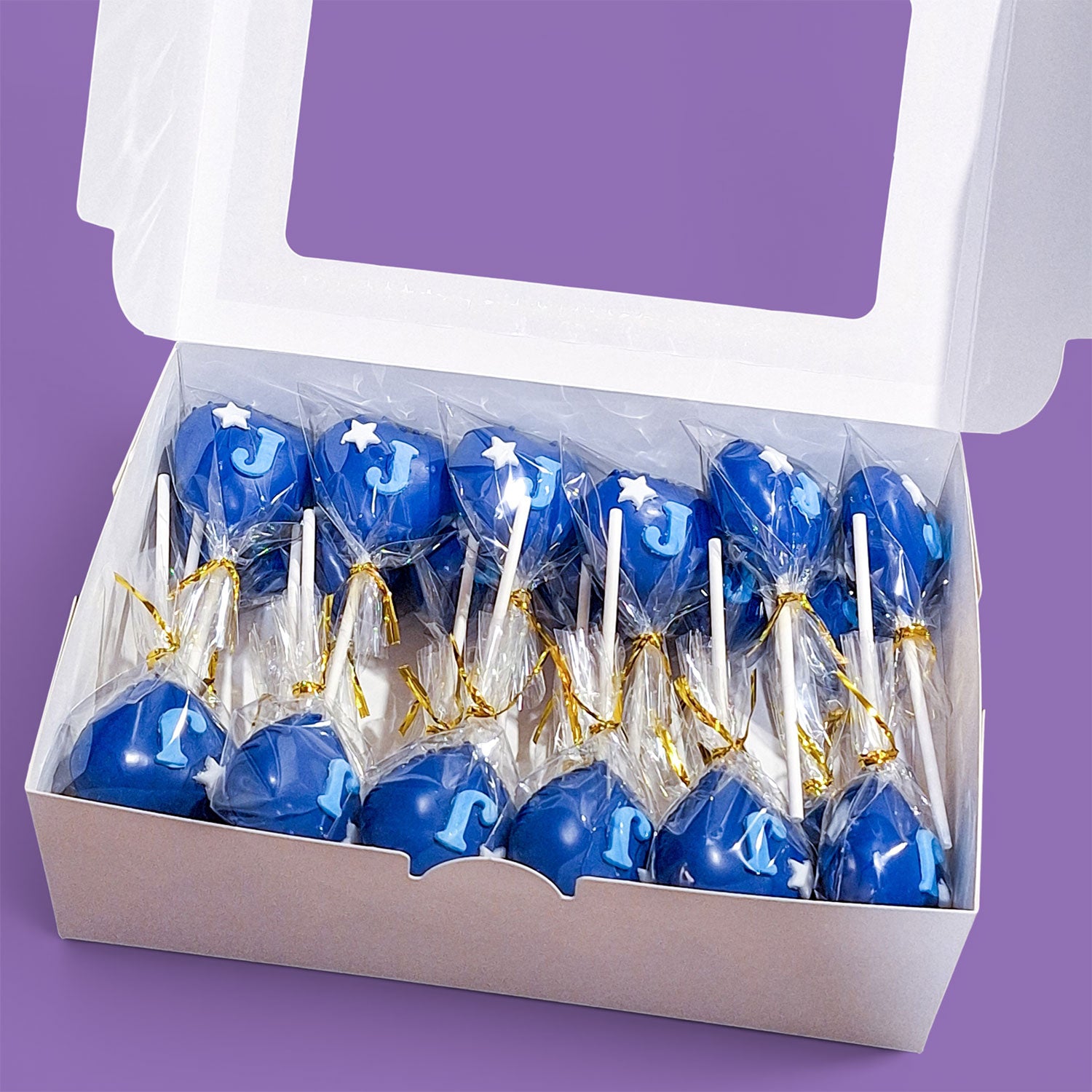 Box of blue heart-shaped Cake Pops with 'J' and white stars.