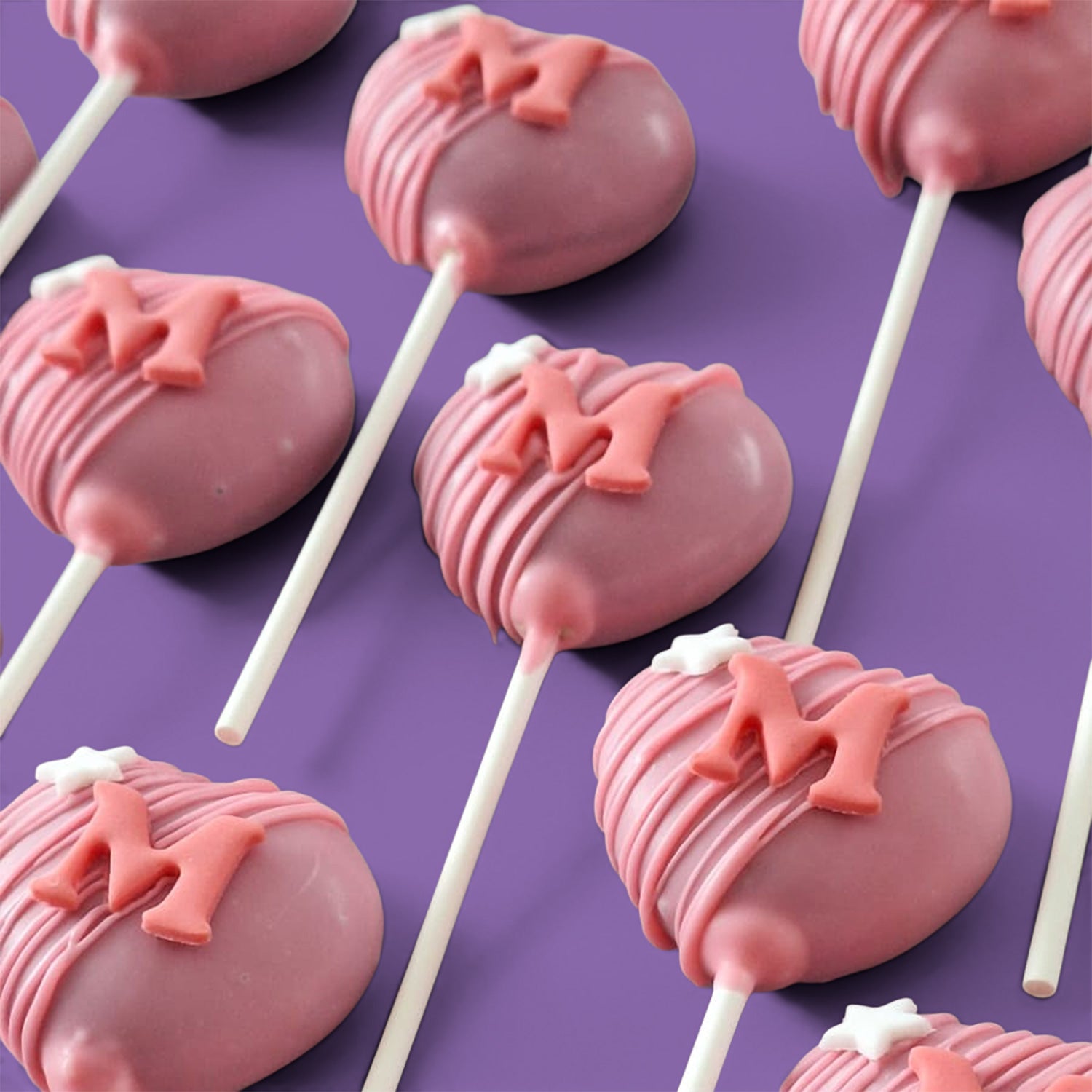 Pink Heart-shape Cake Pops with letter 'M' and white stars.