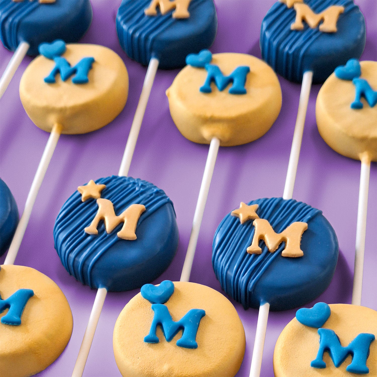 Rounded Blue and Gold Cake Pops with 'M' letters, heats and stars.